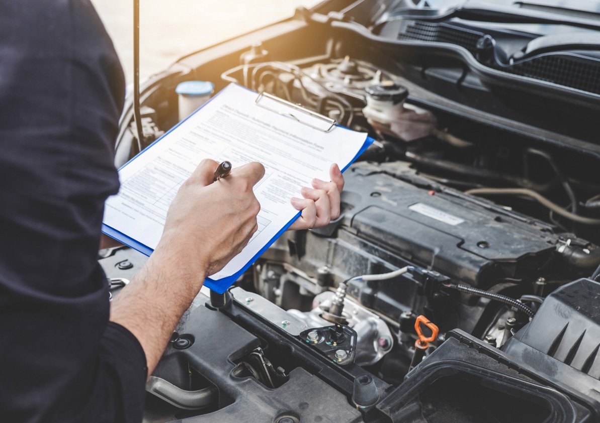 Inspector with a clipboard looking under a car hood.