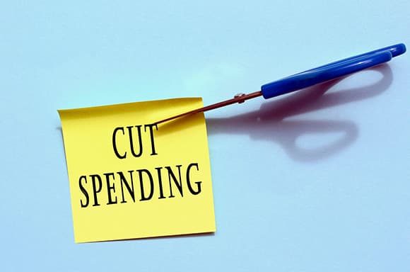 Image of scissors cutting a sticky note, that says cut spending.