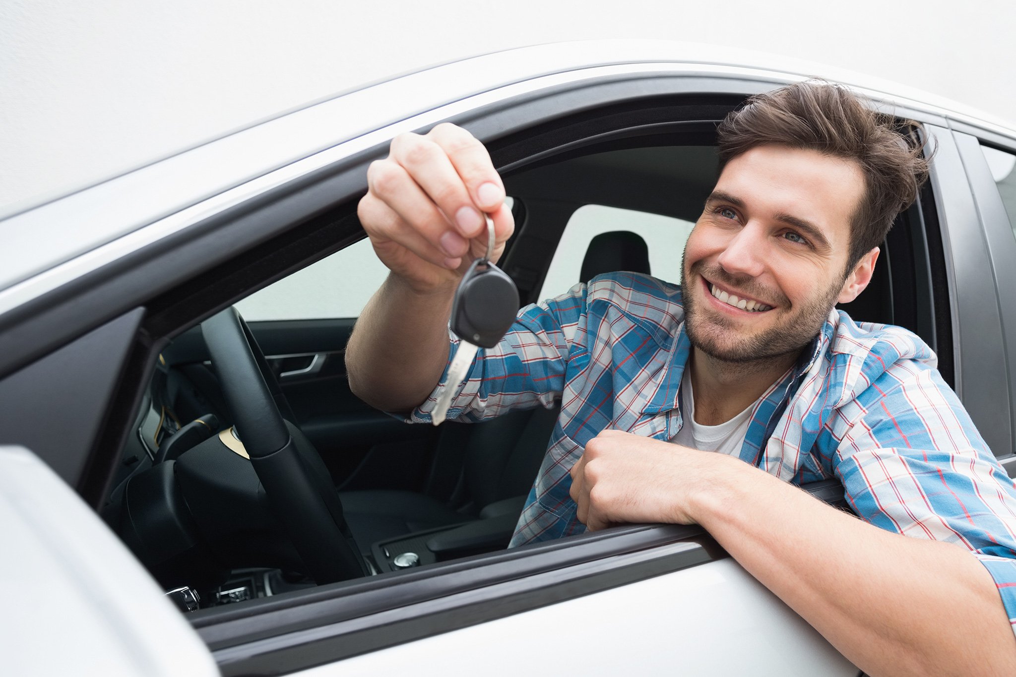 Young man smiling and holding the key of the car he's selling.